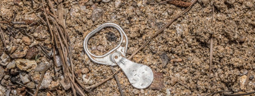 Old aluminum pull tab on sandy ground, a reminder that small actions can create peace of mind.